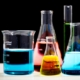 A collection of glass beakers, Erlenmeyer flasks, and graduated cylinders containing colorful liquids.