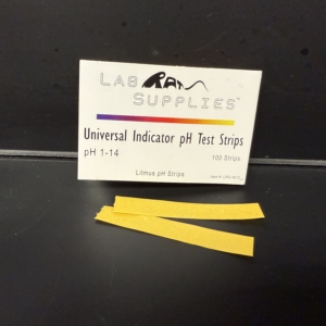 Lab Supplies pH strips A small white book labeled ‘Universal Indicator pH Test Strips’ with two yellow test strips placed in front of it on a black countertop. Alternative text created using Copilot and edited by a human on February 26, 2026.